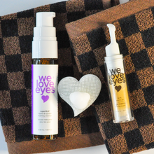Load image into Gallery viewer, Two skincare bottles labeled 'we love eyes' on a checkered fabric background