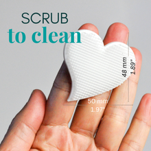 Load image into Gallery viewer, Heart-shaped cleaning scrubber held between fingers with measurements and text 'SCRUB to clean' on a gray background.